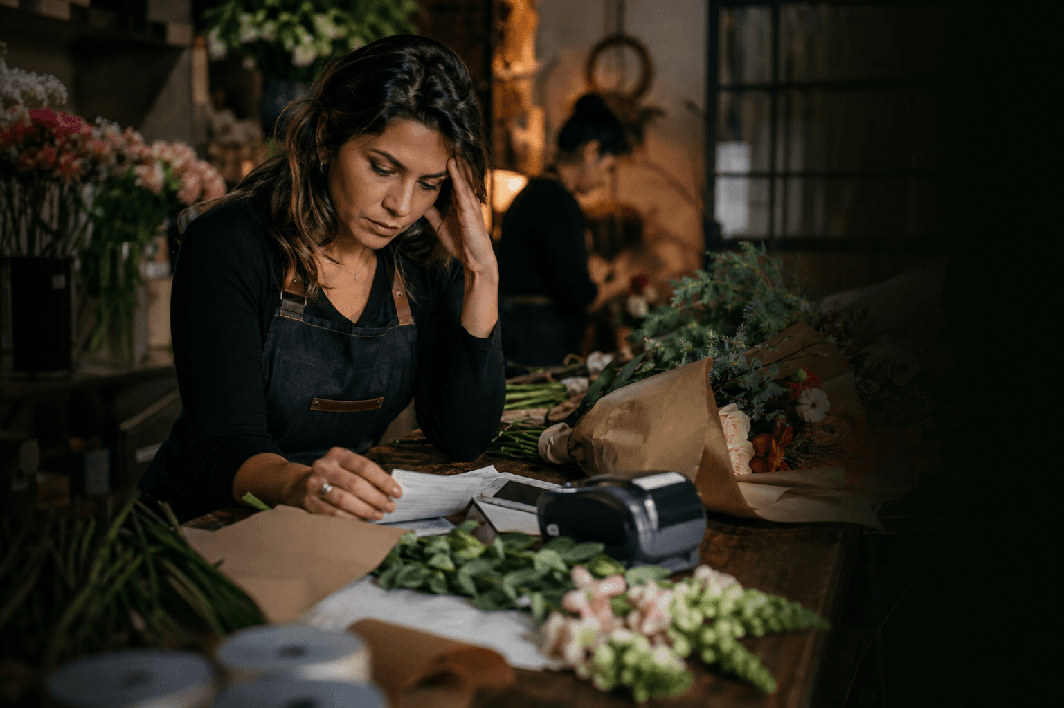 Empresária de floricultura preocupada enquanto confere os pedidos do dia